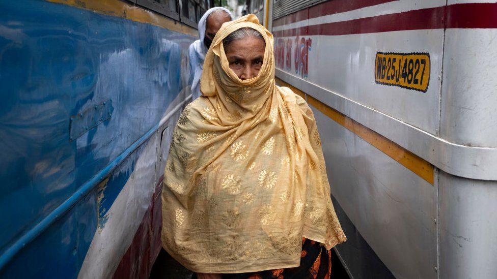An old woman without wearing a safety mask covered her face with a cloth, crossing through the lane of a city bus terminus in Kolkata, India on July 1, 2021. West Bengal Govt has given certain restrictions on the lockdown effective from 1st july to 15th july. Bus, auto and toto services has been resumed with 50% capacity. Saloon, parlour and gym can be opened with 50% customers. Local train and metro will not be operational as per the Indian media report. Though the bus services were not regular as bus service unions protest to hike the bus fare and appealed for compulsory vaccination for all bus service operators. (Photo by Dipayan Bose/NurPhoto via shabby pictures)