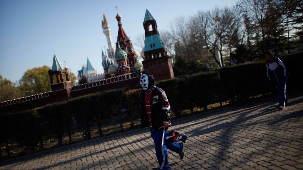 A boy in a mask walks past a replica Kremlin in Beijing World Park, 23 November 2012.