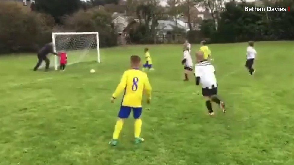 A dad about to push his goalkeeper son to stop the ball going into the net