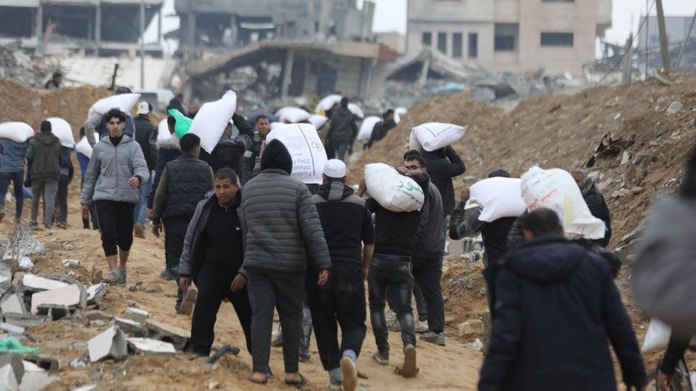 Palestinians carrying bags of grain in Gaza, Feb 2024