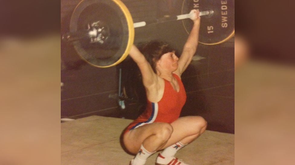 A photo from Trish taken in the 90s where she is squatting whilst holding a barbell above her head