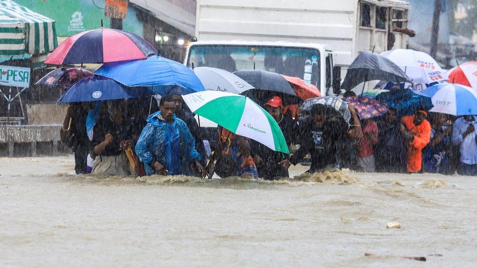 People knee-deep in flood water, holding umbrellas