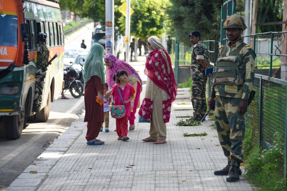 Kashmiri residents walk next to Indian troops standing on guard in Srinagar.