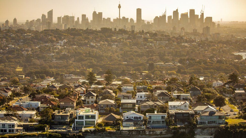 Аэрофотосъемка горизонта Сиднея с пригородом и домами на скале прибрежного моря на переднем плане.