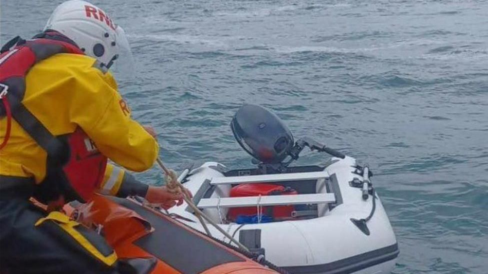 RNLI crew pulling a small white inflatable boat to a lifeboat