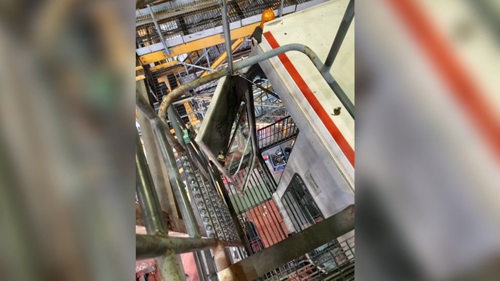 A photo looking down into a hole in the floor of a piece of equipment with a large drop and a metal grate below it