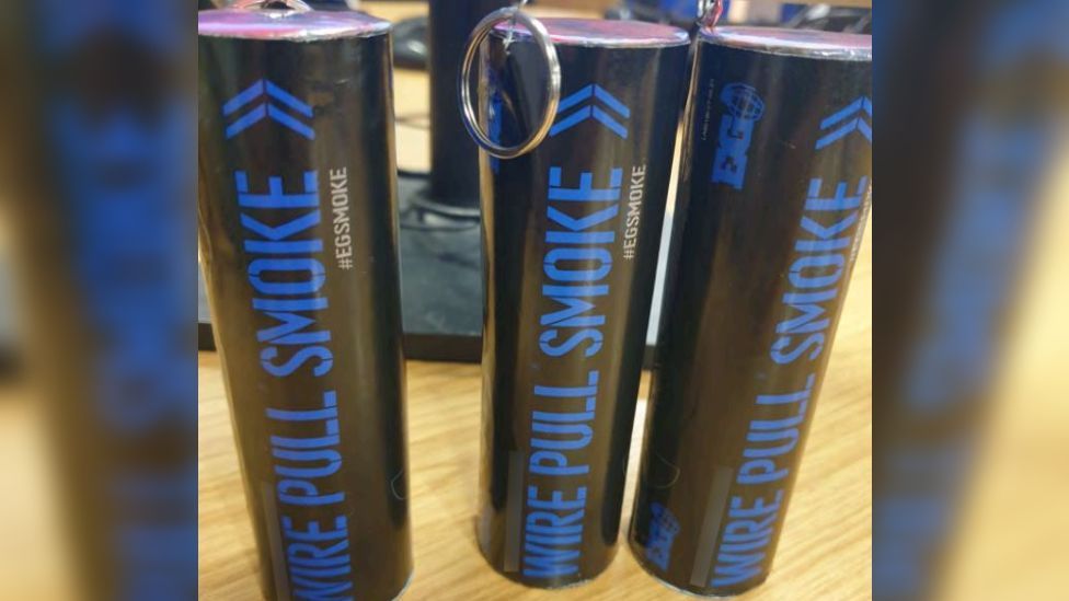 Three black cylindrical flare cannisters with blue writing that says 'wire pull smoke'