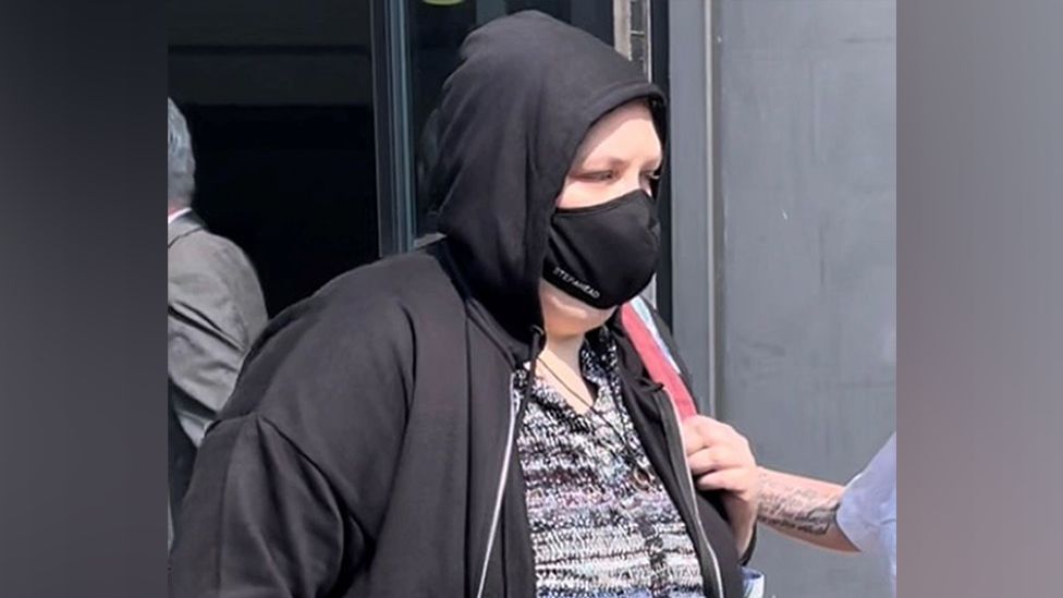 Holly Le Gresley wearing a black Covid-style face mask walking out of court in a black hoodie