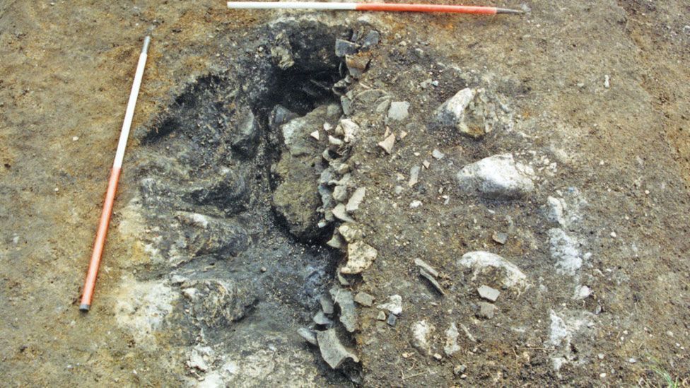 An excavation showing layers of broken or flattened ceramics on the right and large rounded jar shapes on emerging on the left