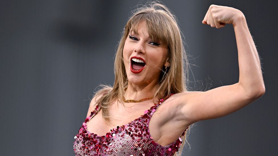 Taylor Swift curling her arm and balling her fist in a red sequined outfit