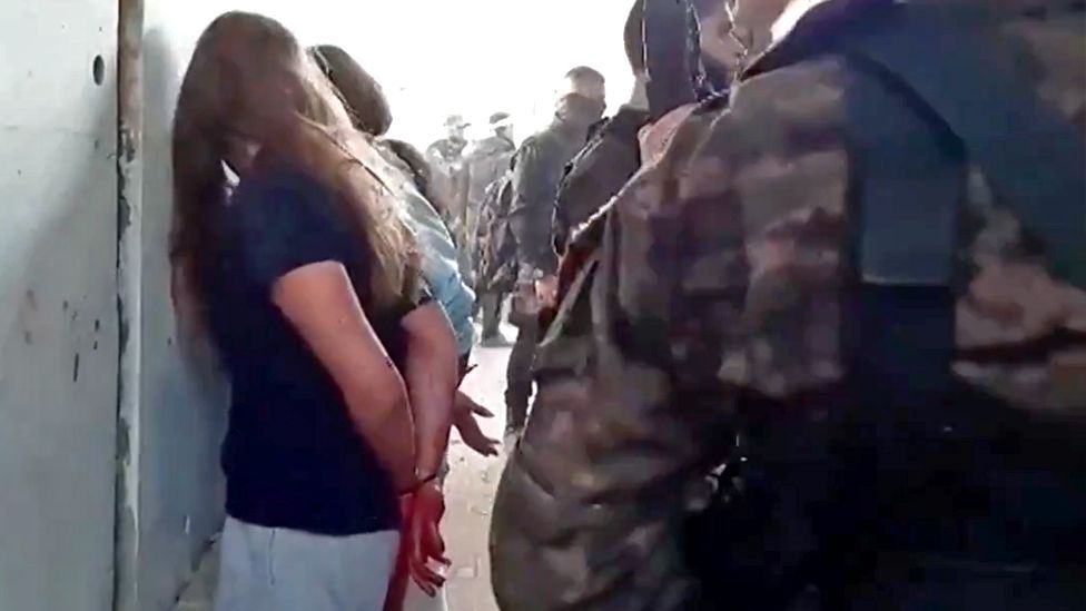 Israeli hostage Naama Levy (L) is seen with her hands bound and facing a wall as Hamas gunmen stand next to her in the newly released video filmed by Hamas gunmen at Nahal Oz base on 7 October (22 May 2024)