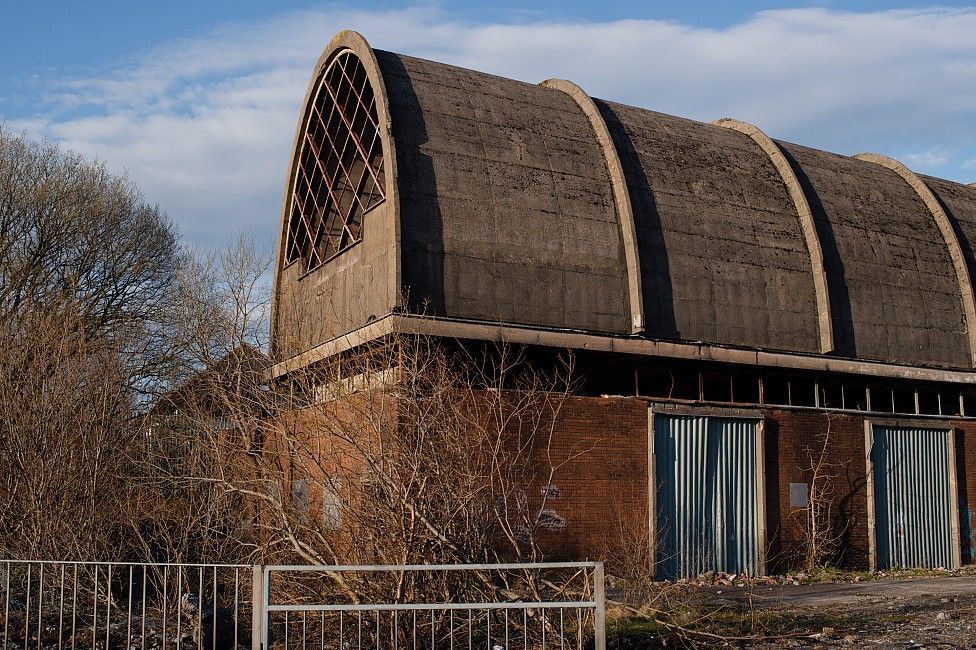 A high arched roof building with with corrugated iron covering doorways, and rubble outside