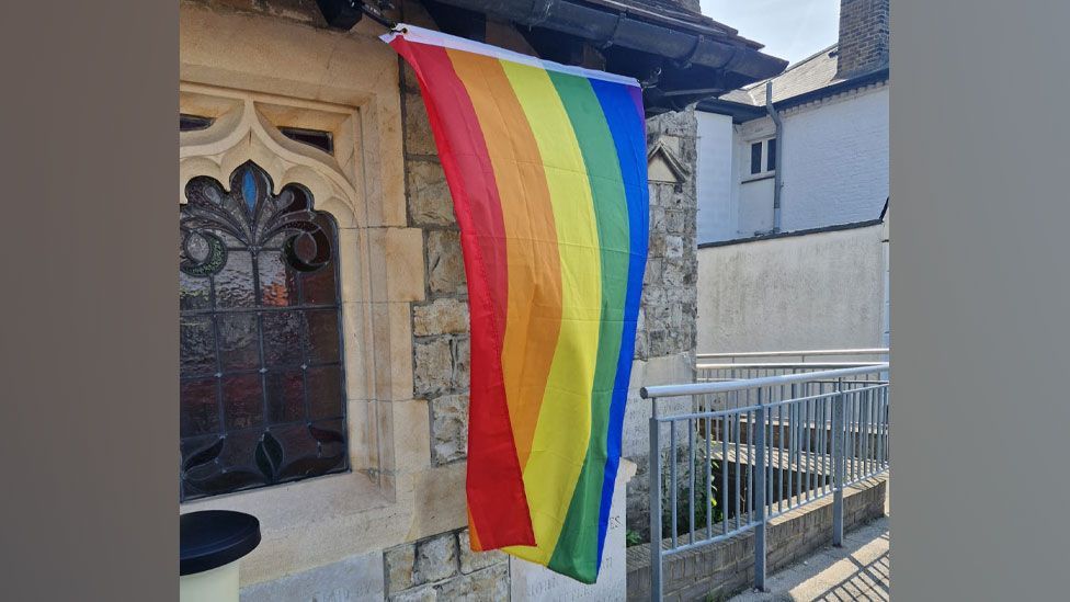 Rainbow Pride flag fluttering on the wall of the stone-built  Methodist Church, Leigh, Essex