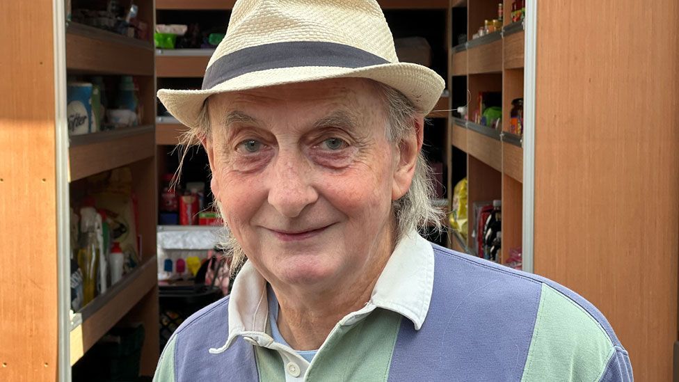 A man wearing a cream hat over shoulder-length light coloured hair and a striped rugby shirt