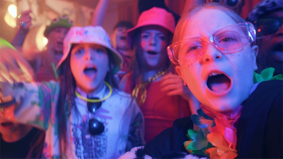 Children in colourful outfits performing The Spark