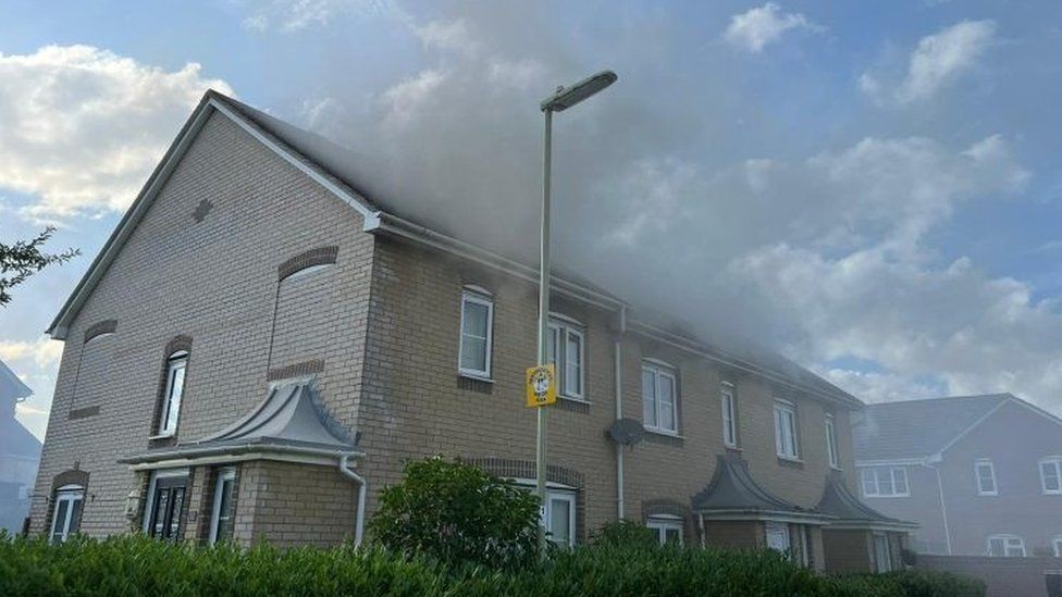 Smoke billowing from the roof at the front of a pale brick, terraced home with white windows