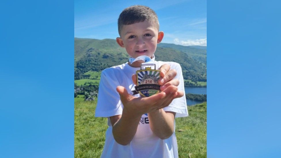 Leo holding a medal which marks him climbing all 214 peaks
