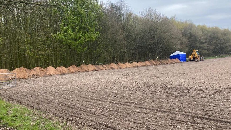 A white and blue police tent in a field lined with trees