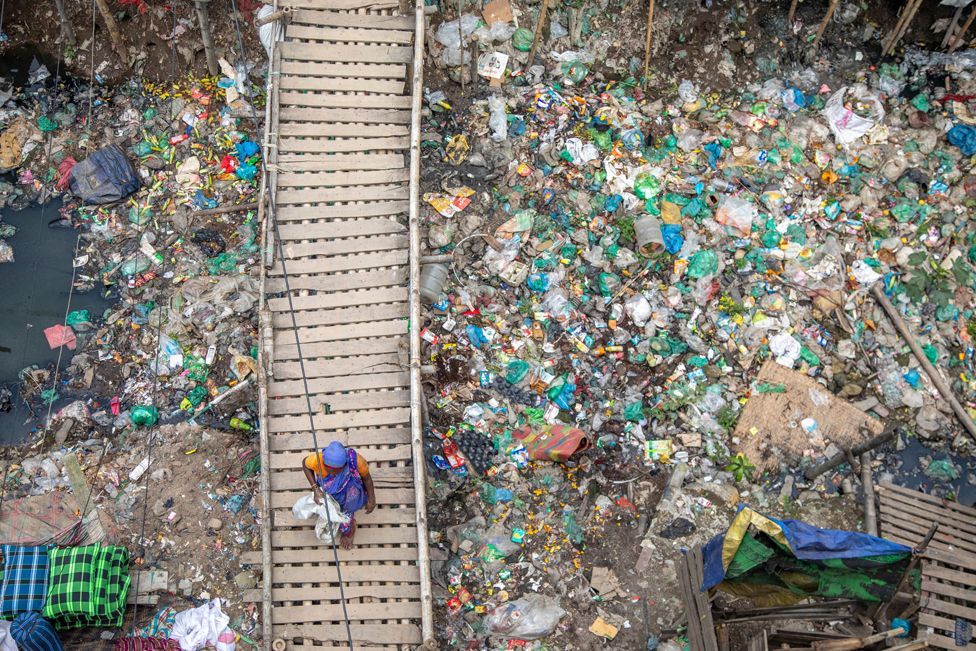 A woman walks on the wooden bridge next to a Kajla canal filled with household garbage in Dhaka, Bangladesh