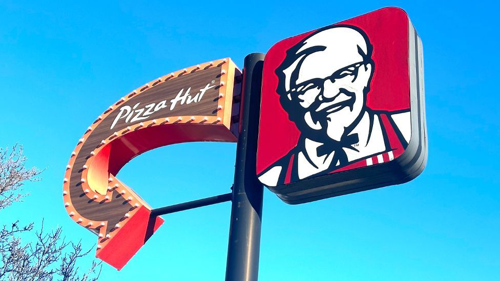 Sign with an arrow for Pizza Hut on the left and the KFC Colonel logo on the right