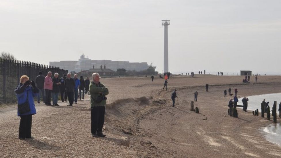 People on beach watch a large container ship passing Landguard Point in Felixstowe