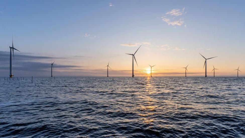 A picture of an offshore wind farm in the sunset