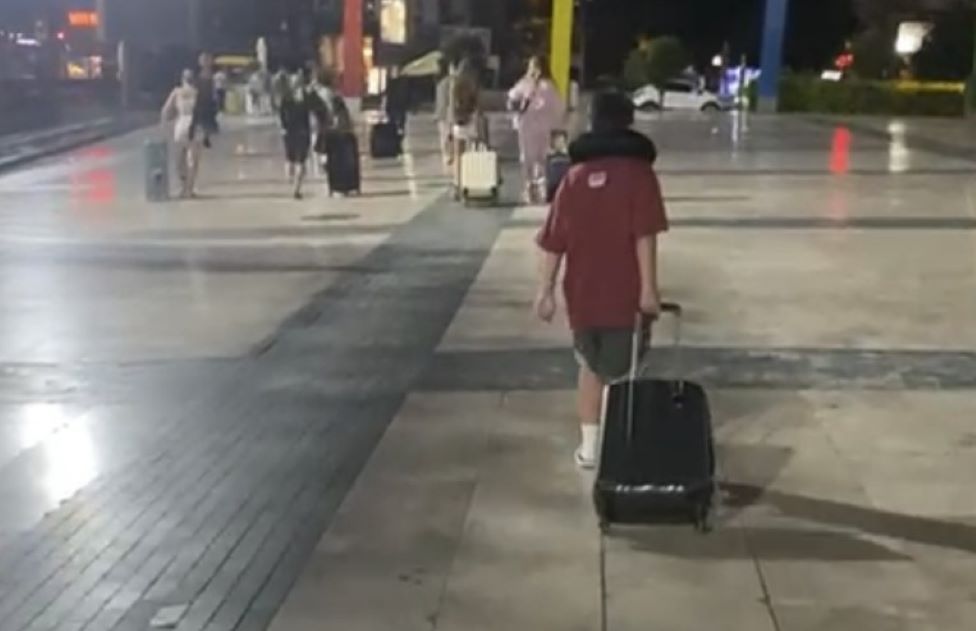 Jodie Tracey's son following a crowd of people wheeling their suitcases as they head to their new hotel