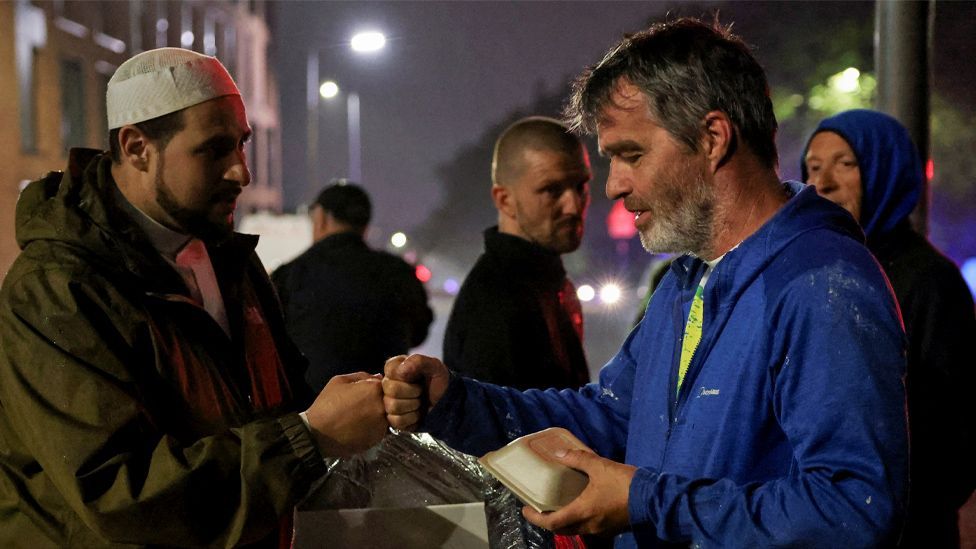 Imam Adam Kelwick fistbumps a protester as he hands out food during a protest