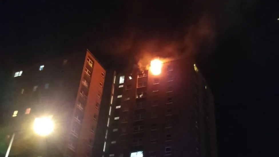 Image of a tower block in Bristol. It is pictured at night. A street light can be seen in one corner and a fire can be seen on the top floor of the flat. 
