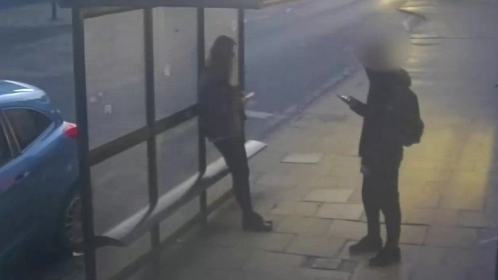 CCTV image showing Holly Newton leaning against a bus stop in Hexham, while the boy who was to attack her is standing a few feet away from her