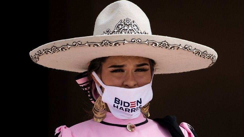 A woman wears a hat and a face mask that reads "Biden Harris"