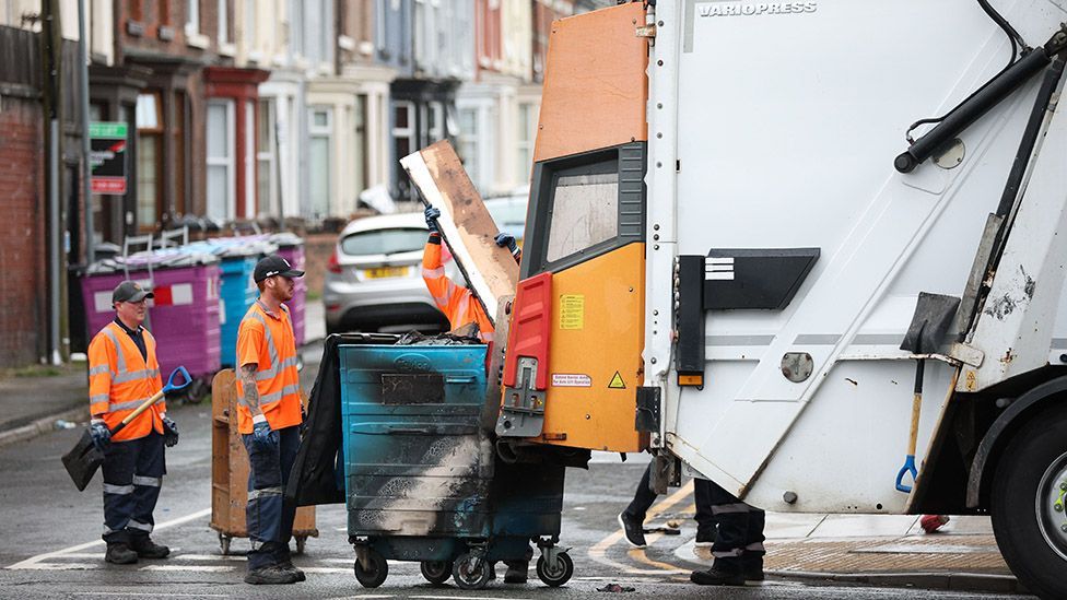 Council workers clear debris from County Road after a night of violent disorder in Liverpoo