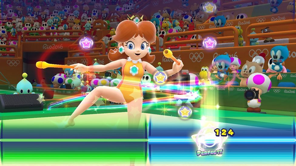 A screenshot shows Princess Daisy wearing a yellow leotard and twizzling two batons as musical button prompts scroll down the screen. A line at the bottom denotes the point at which players must press the button, keeping the rhythm of the tune.