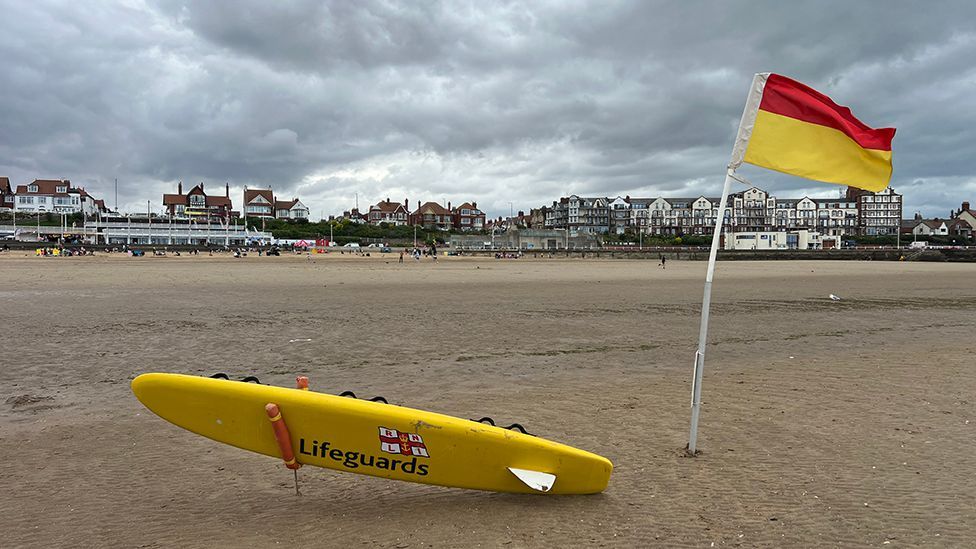 A RNLI paddleboard and yellow and red flag on the sand at Bridlington South Beach