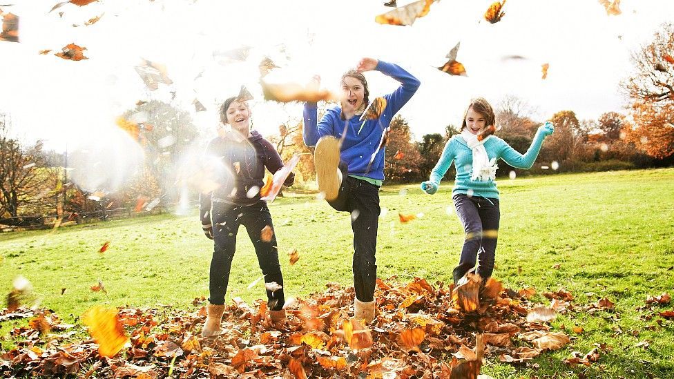 Children kicking up leaves and smiling