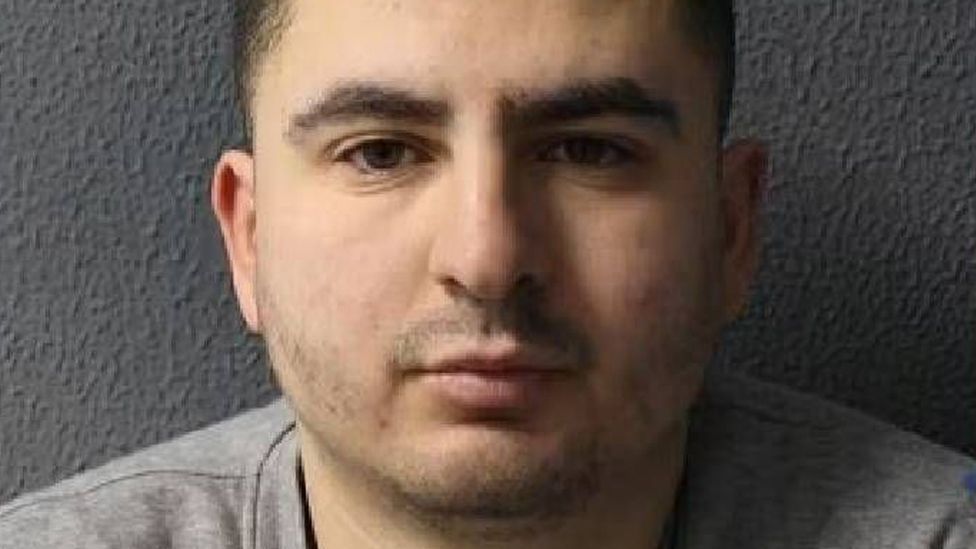 Abderrahmane Ariba, 30, is wearing a light grey t-shirt and is looking directly at the camera. He has dark brown short cropped hair, is unshaven with dark eyes and olive skin.