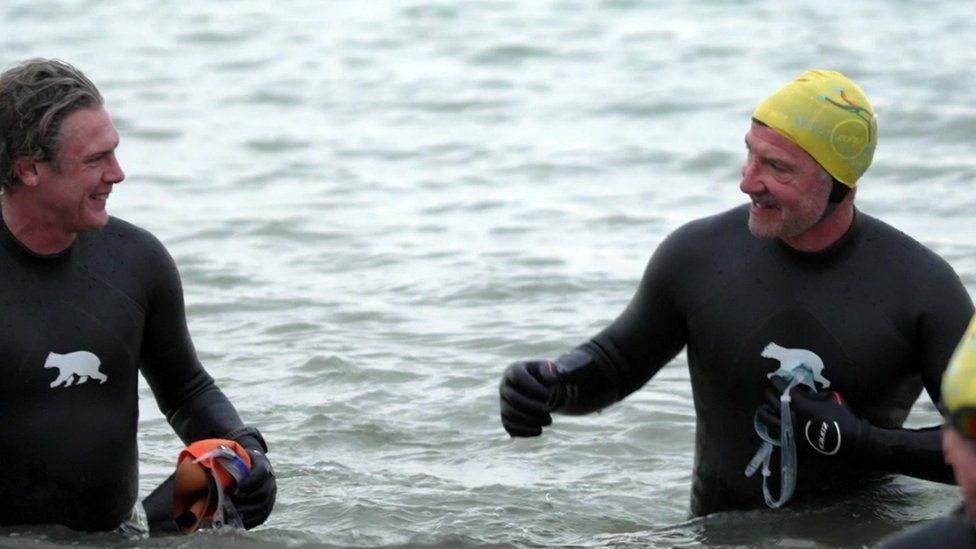 Andy Grist and Graeme Souness wearing black wetsuits and standing waist deep in the sea