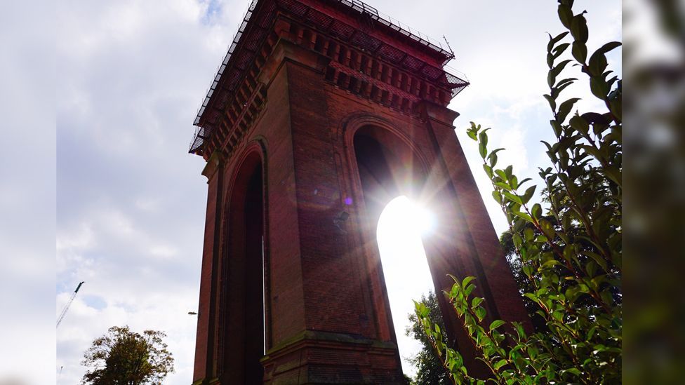 Colchester's Balkerne Water Tower, which is 110ft - or 35 metres - tall. It has four pillars and is made of red brick. The sun is shining in the background.