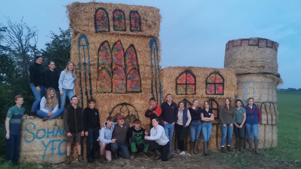 A straw bale sculpture of Ely Cathedral with 19 Soham Young Farmers group members standing in front