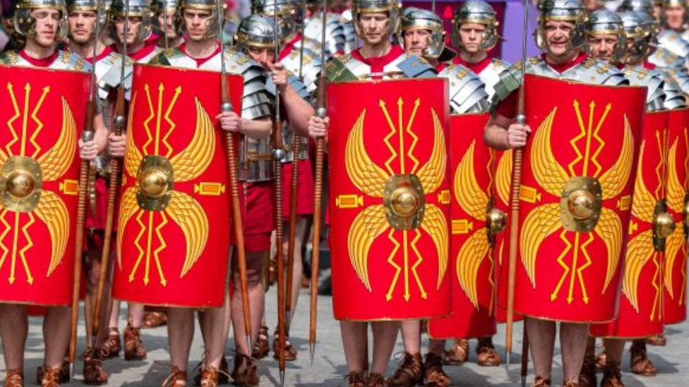 About 15 men dressed as ancient Romans in armour and carrying spears and red and yellow shields