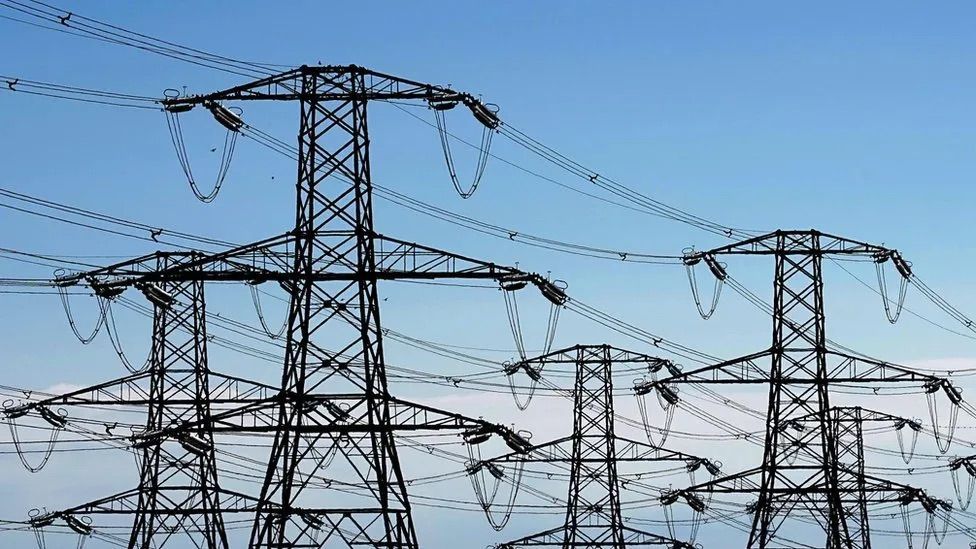 Five electricity pylons set against a light blue sky.