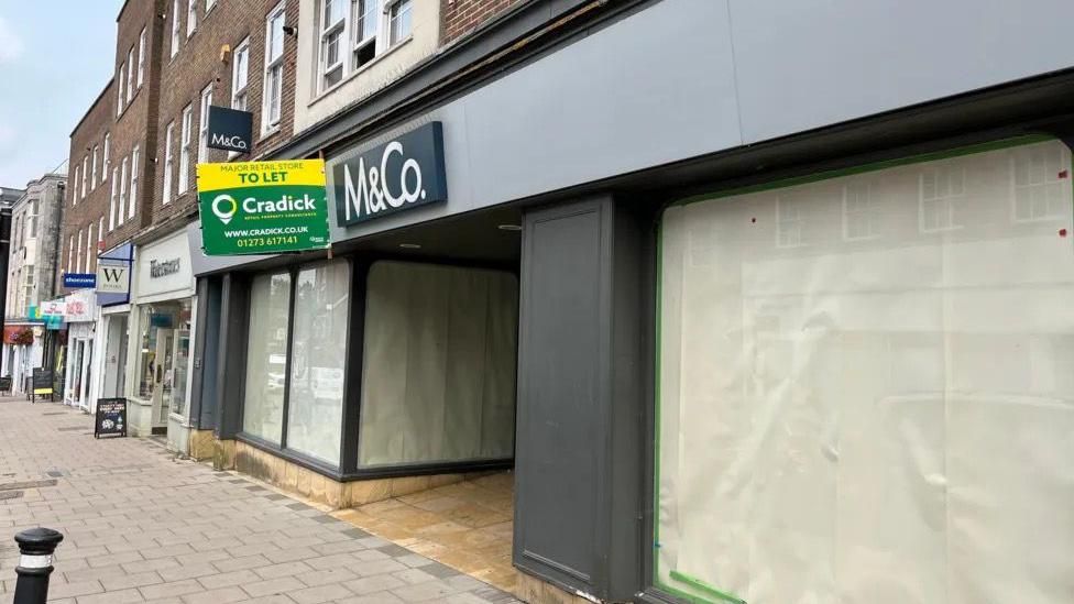 An empty M&Co with sheets in the windows. 