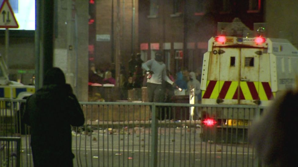 A masked rioter throws bottles at police Land Rovers during Tuesday night's trouble