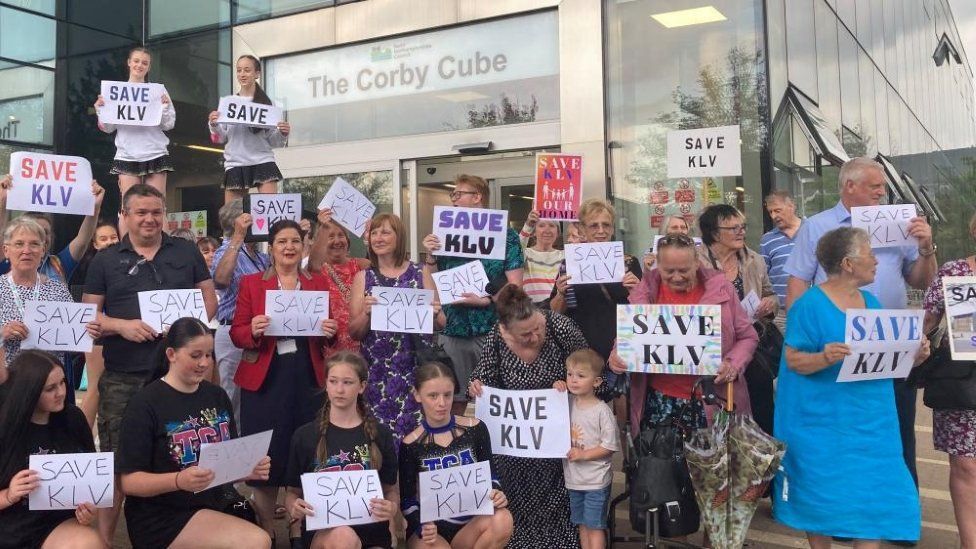 A group of people holding "Save KLV" signs outside the Corby Cube