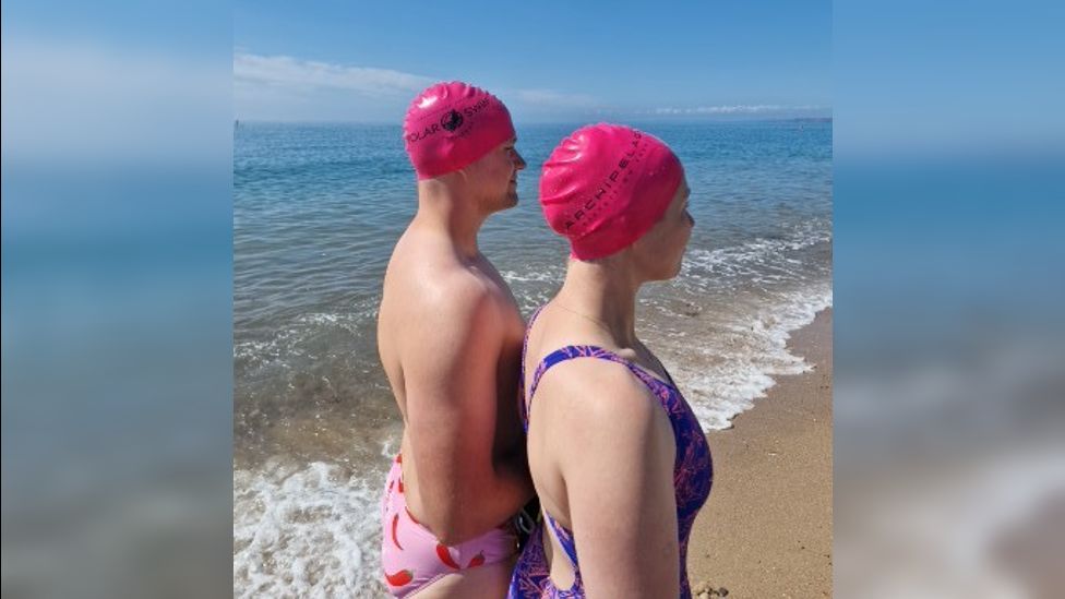 The couple in swimsuits and caps standing on a beach on the shoreline