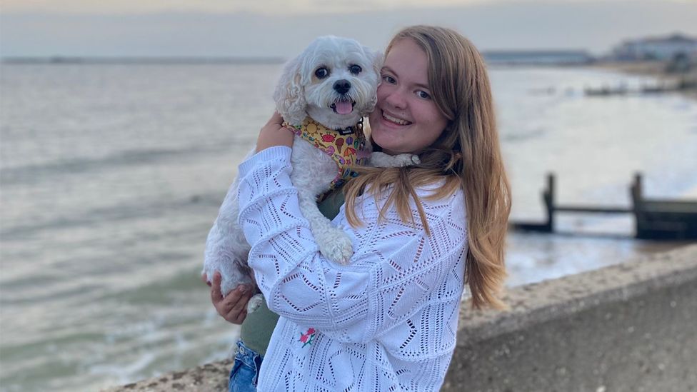 A woman wearing a white knitted cardigan holding her King Charles Spaniel dog 