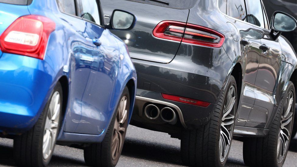 A blue car close to the bumper of a black car with a glimpse of a car further ahead