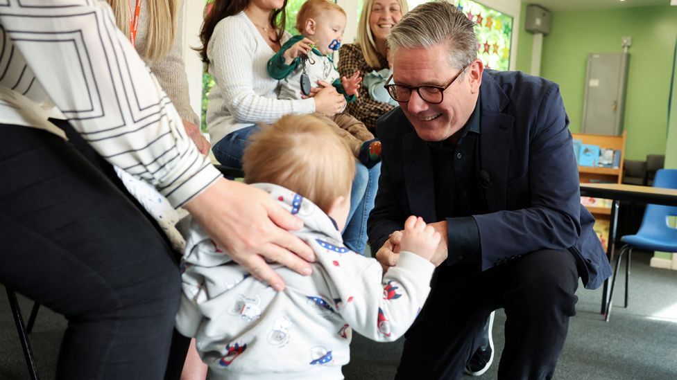 Labour leader Sir Keir Starmer kneels down to greet a toddler at a school in Nuneaton