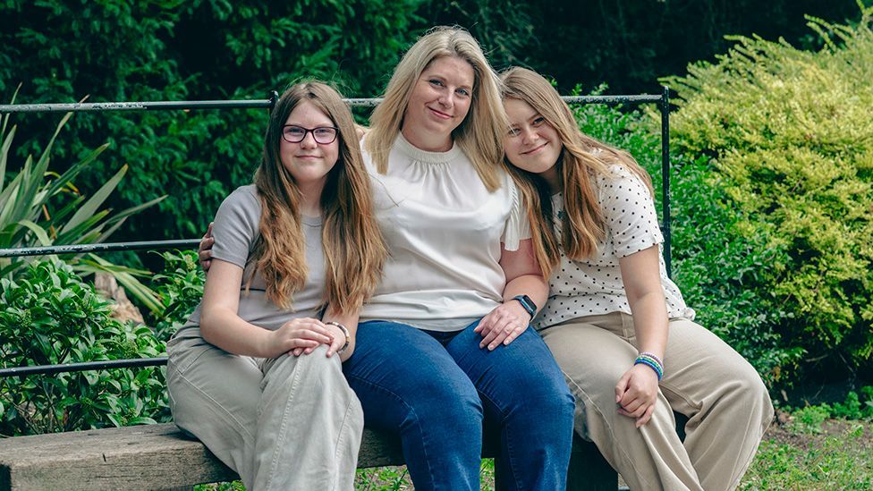 Charlene sitting on a parkbench with her two daughters, Isla and Skye