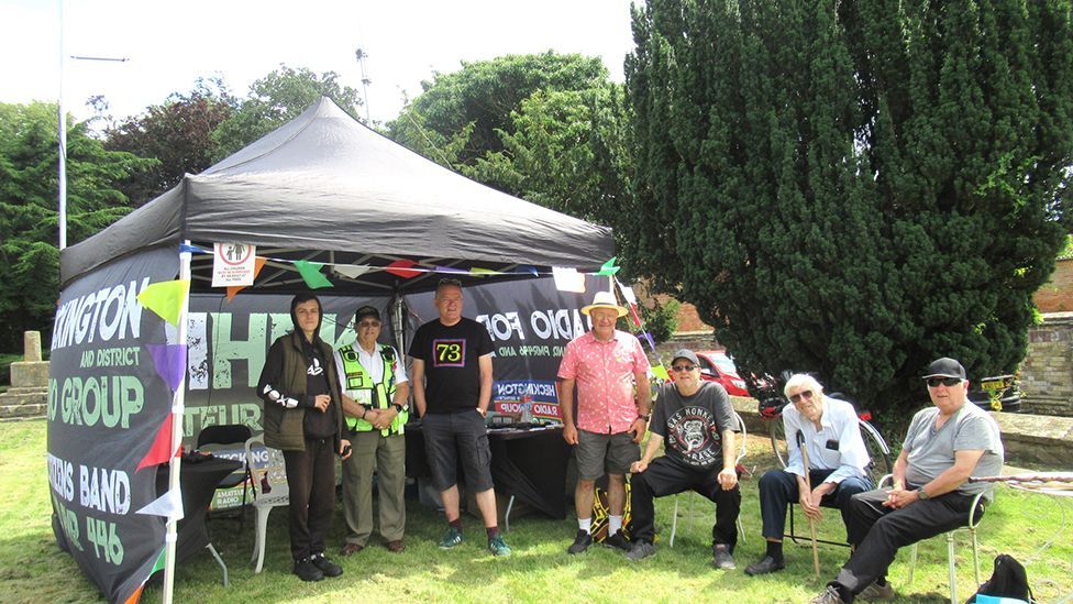 A group of Heckington and District Radio Group members, all men wearing casual clothes, outside a branded marquee at an event.